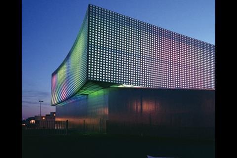 The pyramidal glass block set into the facade of this multipurpose building in Aurillac, France, intensifies the coloured lighting